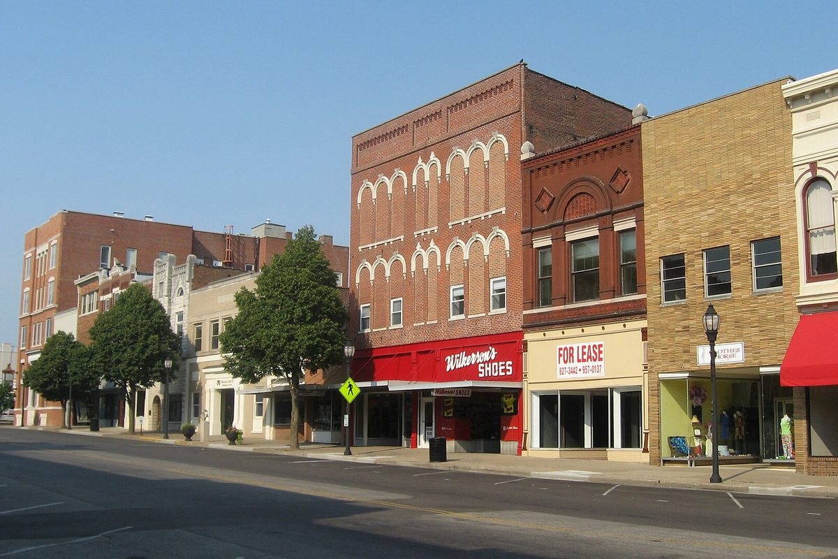 Brick storefronts on North Main Street in downtown Henderson, with Wilkerson's Shoes under a red awning and a For Lease sign next door, on a clear morning