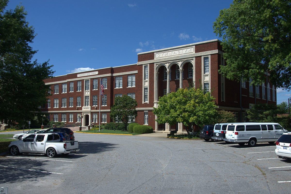 The red-brick Claremont school building in Hickory with a columned entrance and a gymnasium sign, cars parked in the lot in front