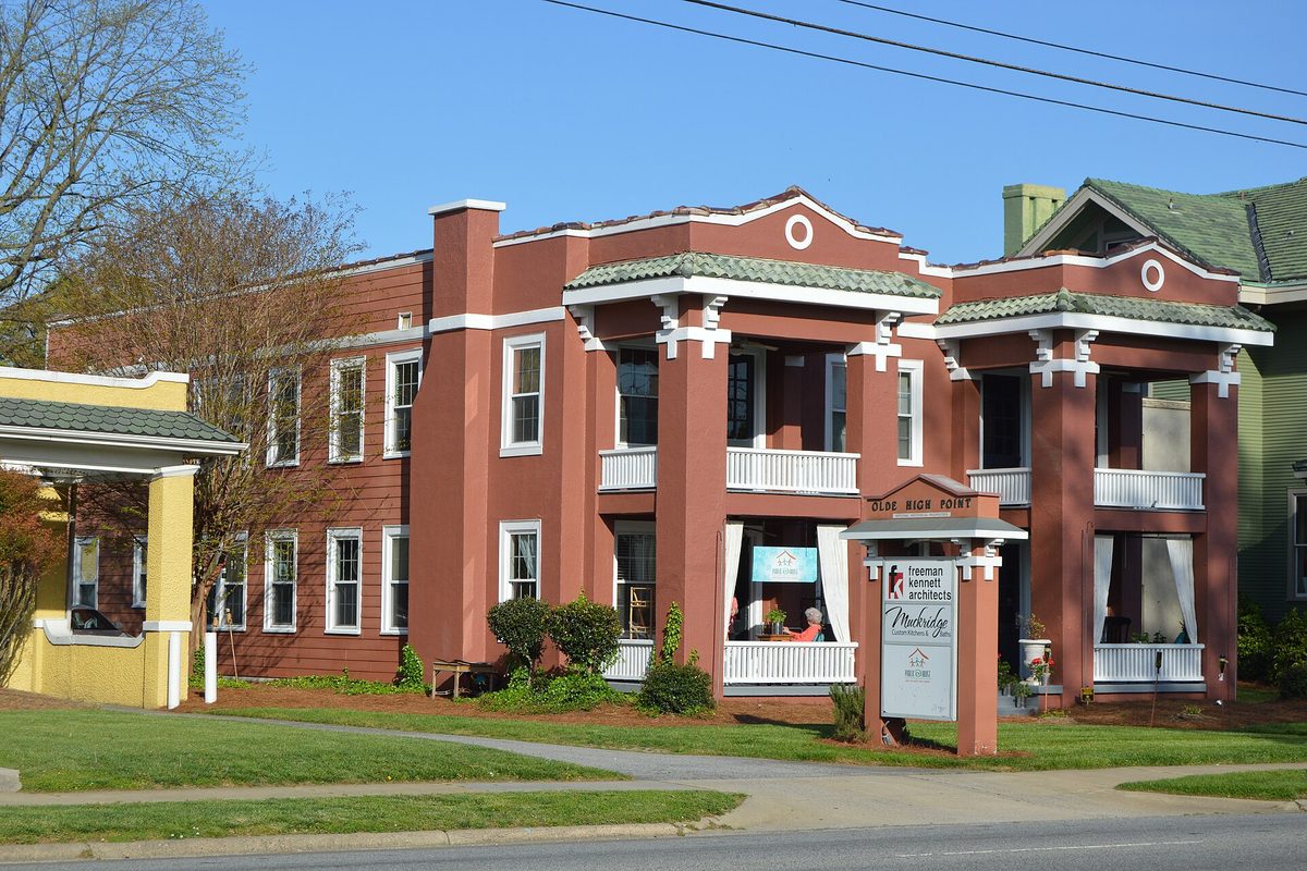 The two-story Hardee Apartments on North Main Street in High Point, painted brick red with white porch railings and columns, behind a small lawn