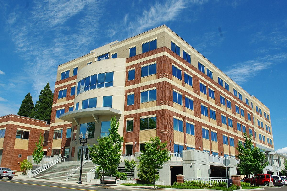The Hillsboro Civic Center, a five-story brick and tan office building with blue windows and a rounded corner entrance, under a blue sky