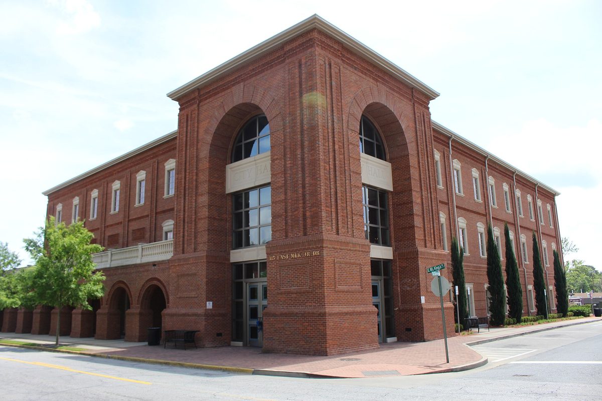 Hinesville City Hall, a three-story red brick building with a tall arched entrance and rows of windows, on a street corner