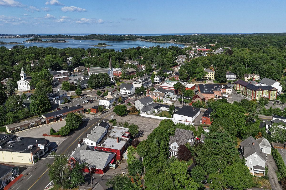 Aerial view of downtown Hingham, with church steeples, rooftops and trees running down to the harbor and its islands