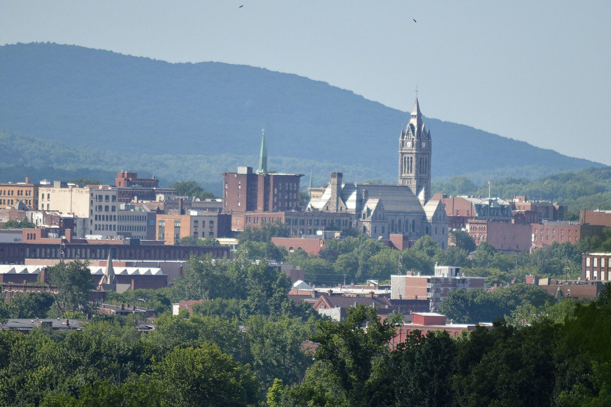 Holyoke's brick downtown with a tall stone church tower and a green spire, and the wooded Mount Tom Range rising behind