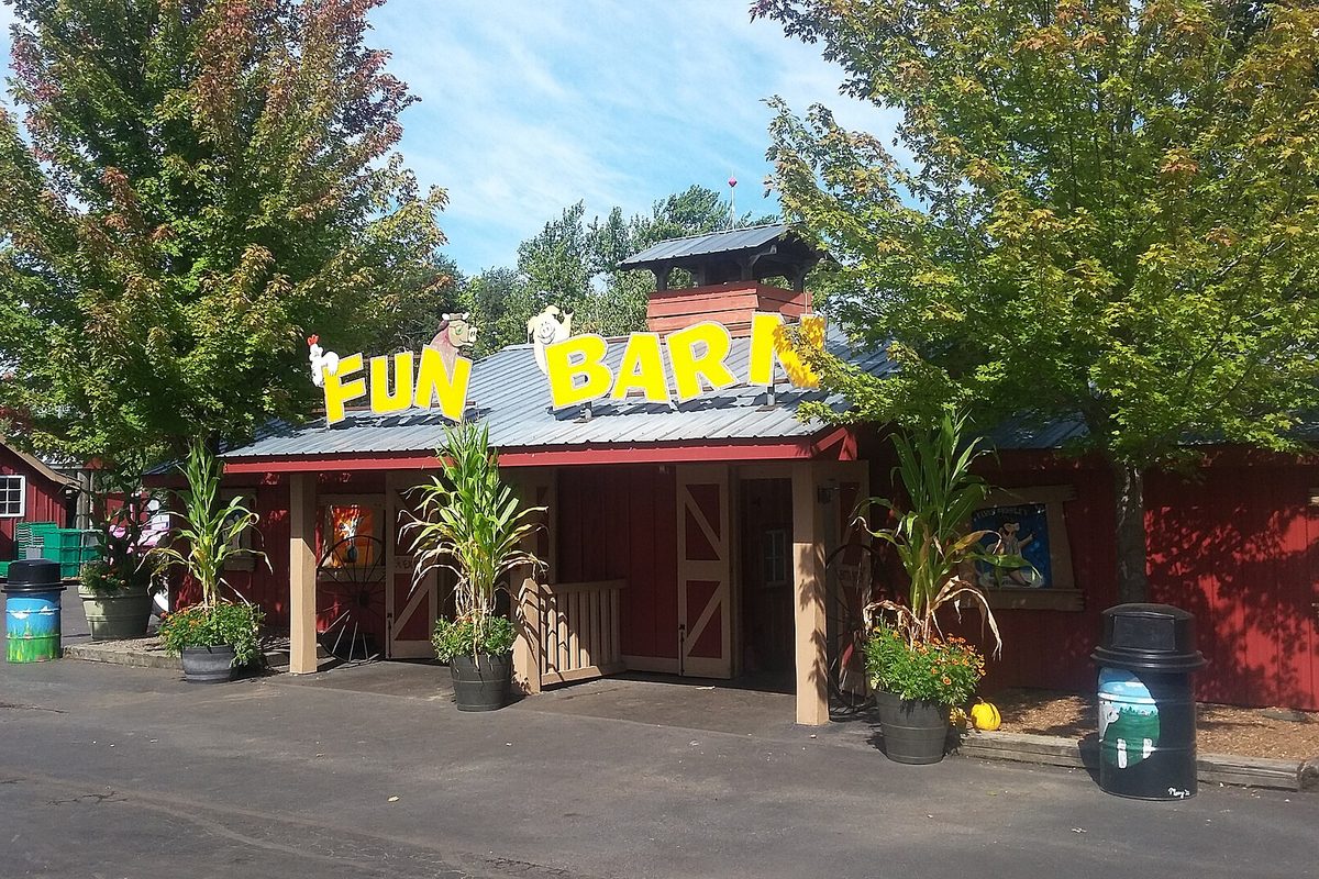 The red Fun Barn at Bengtson's Pumpkin Farm, with big yellow letters on the roof, potted corn stalks by the door and green trees behind it