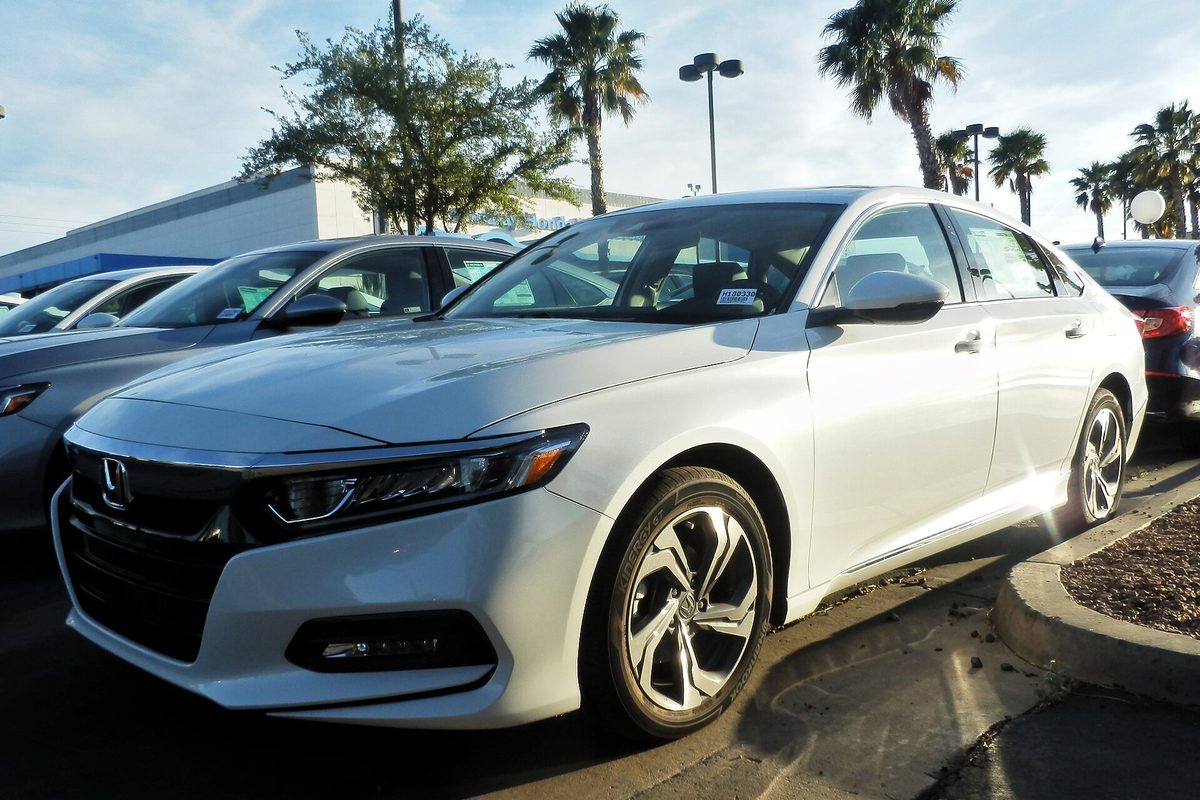 A white 10th-generation Honda Accord sedan on a sunny dealer lot lined with palm trees