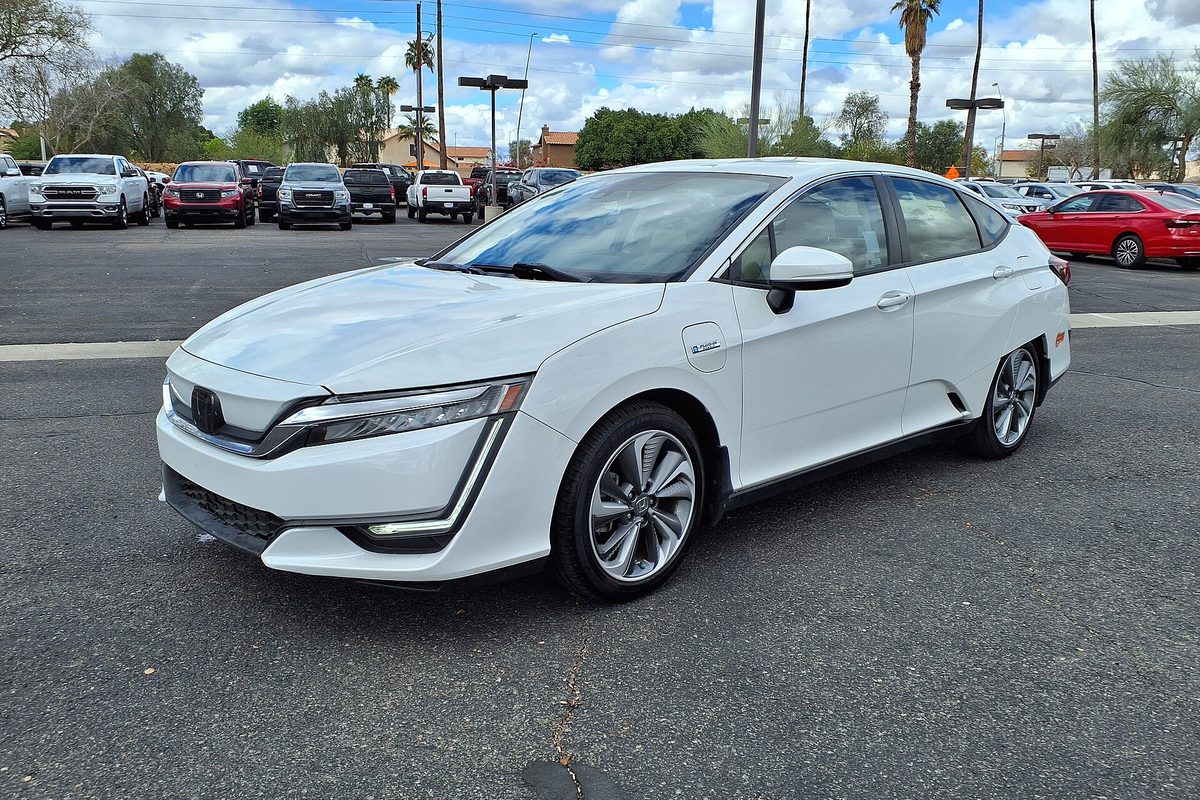 A white 2019 Honda Clarity Plug-in Hybrid sedan on a dealer lot, with palm trees and a cloudy sky behind it