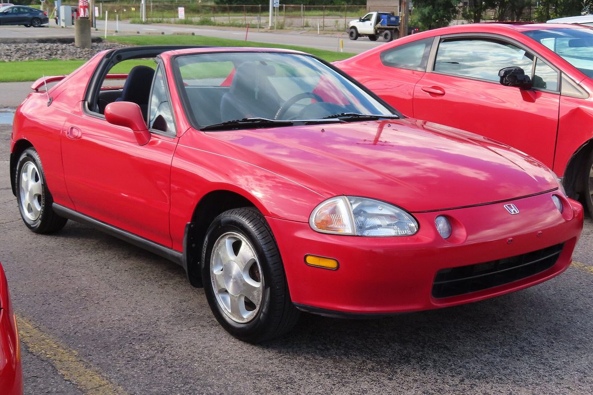A red 1993 Honda Civic del Sol Si with its targa roof off, parked on asphalt next to another red car