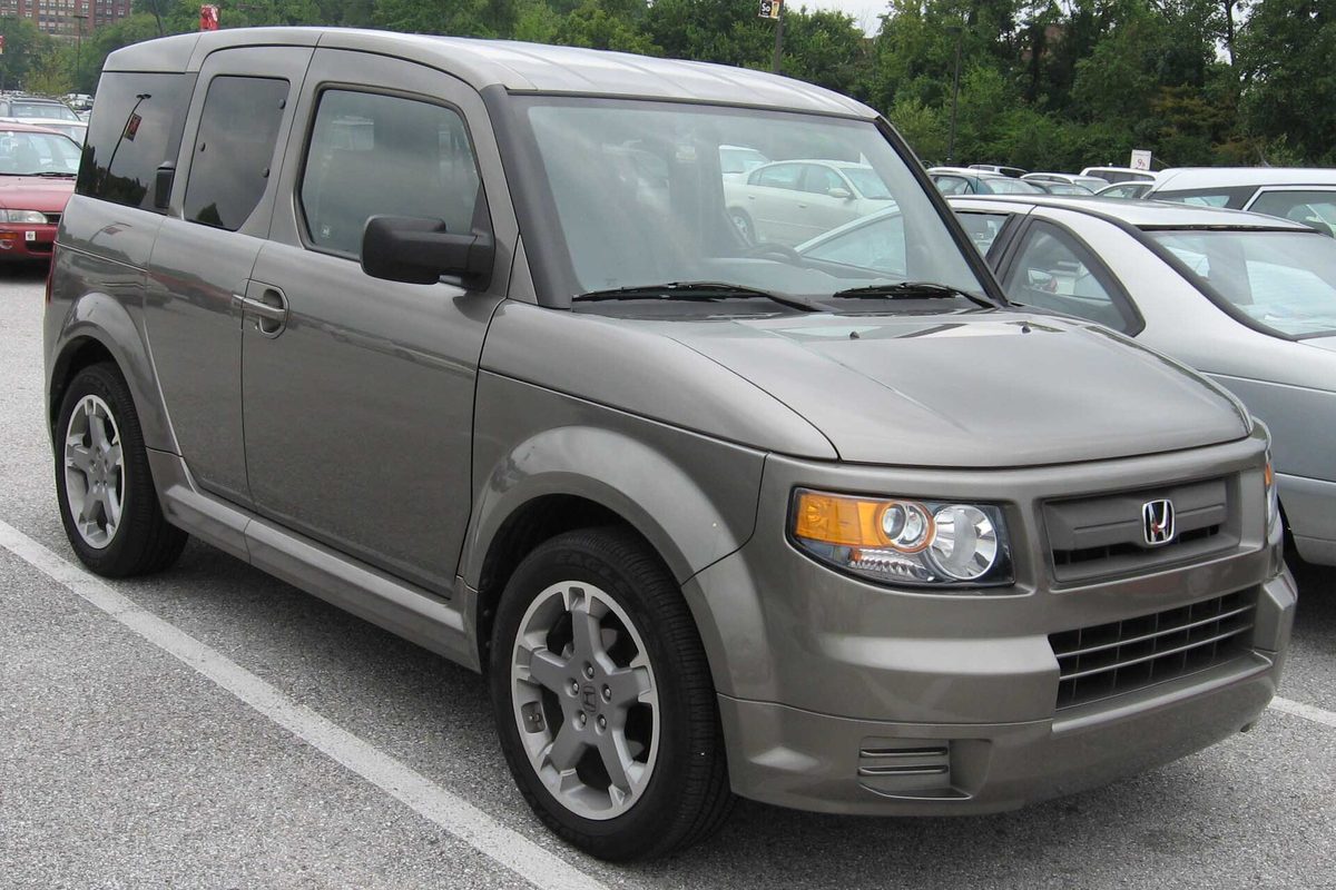 A gray-brown Honda Element SC with silver alloy wheels parked in a striped lot beside a silver sedan