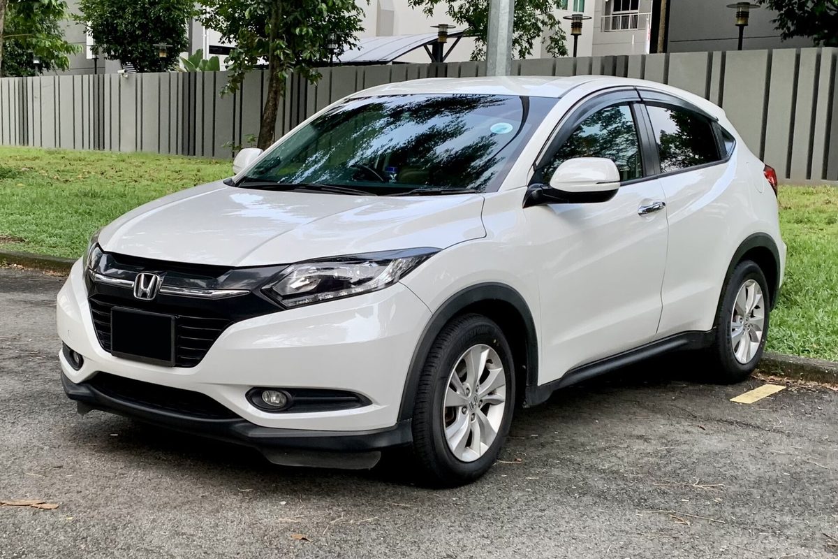 A white Honda HR-V in the body style sold in the US from 2016 to 2022, parked on asphalt beside grass and a gray fence