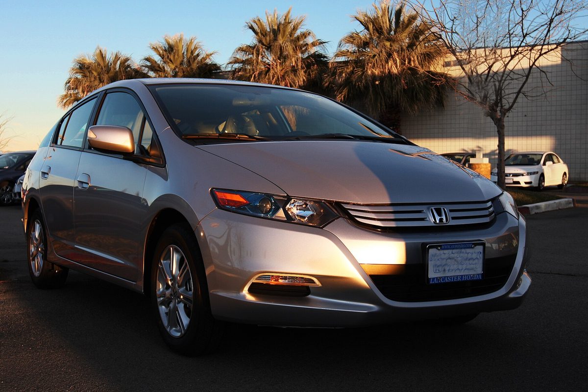 A silver 2011 Honda Insight hatchback in low evening sun, with palm trees and a bare tree behind it