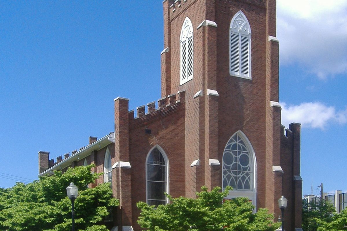 The red brick First Presbyterian Church in Hopkinsville, with a tall square tower, pointed arched windows and white trim behind green trees