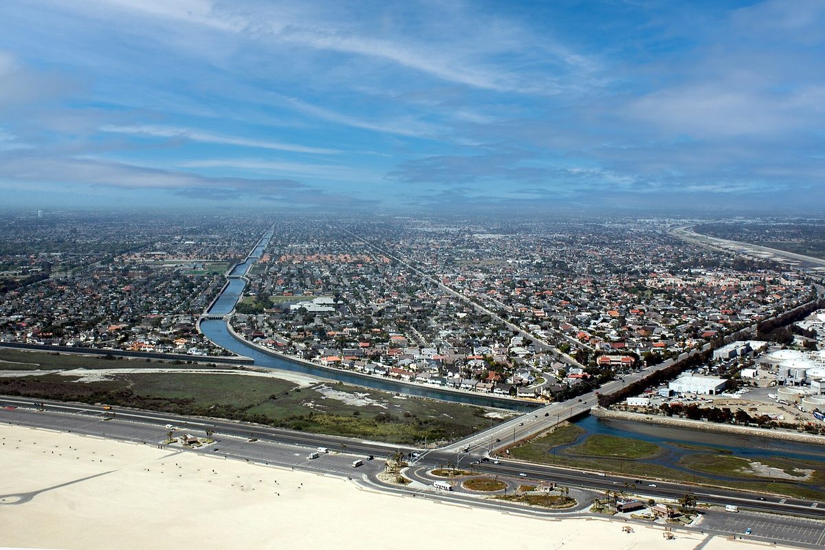 Aerial view over the sand at Pacific Coast Highway and Brookhurst Street in Huntington Beach, with a flood channel and rows of houses running inland