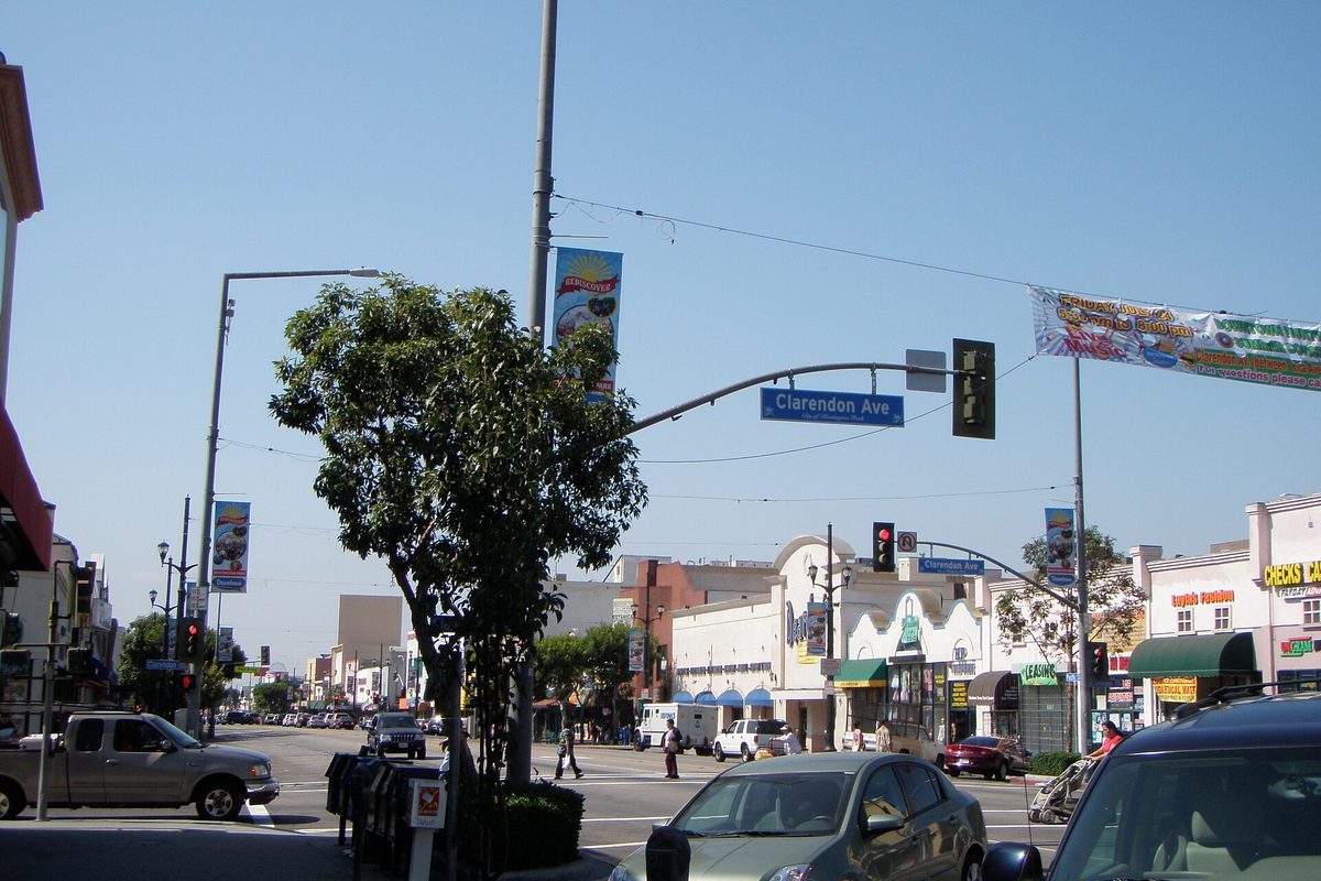 Pacific Boulevard at Clarendon Avenue in Huntington Park, with shop fronts, street banners, traffic lights and parked cars on a sunny morning