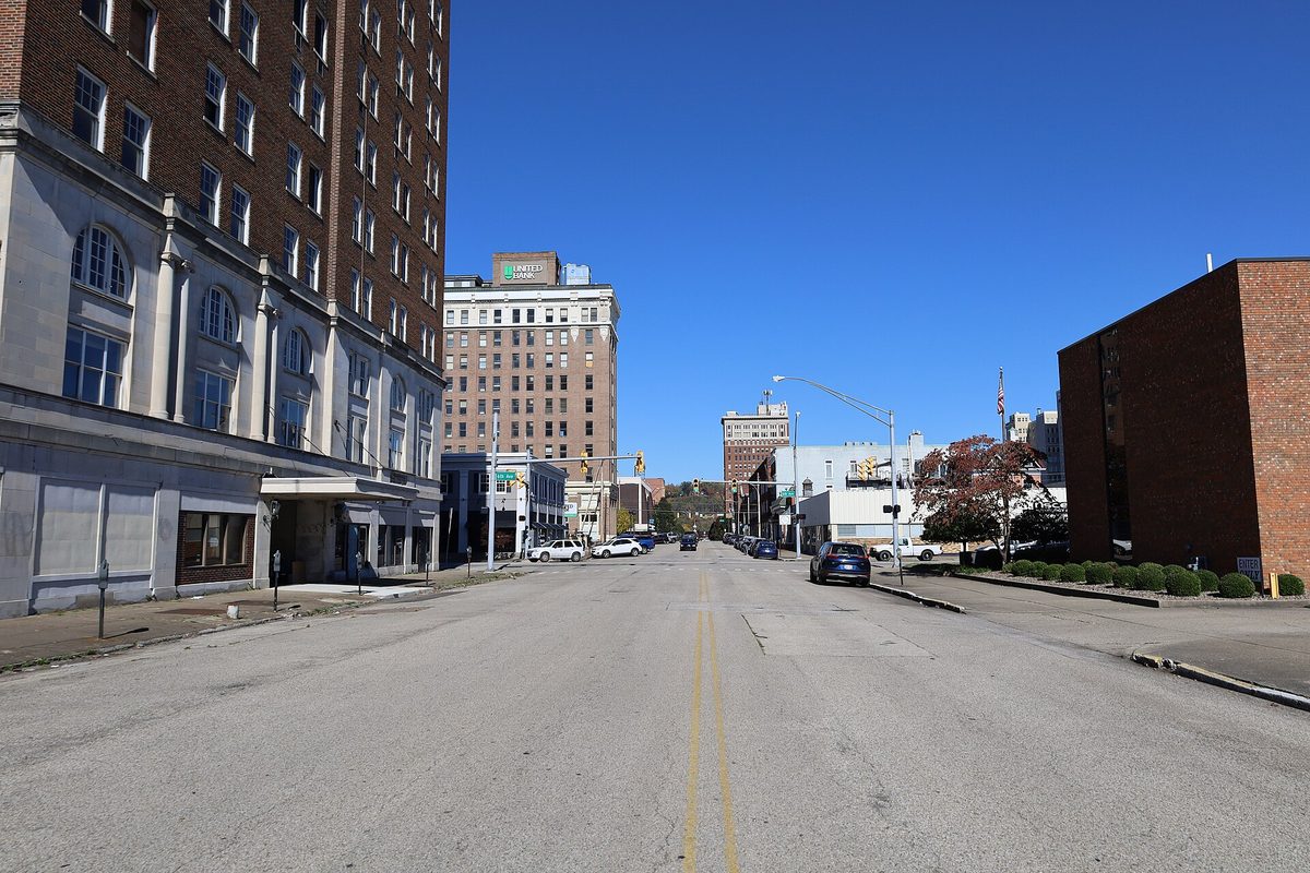 A quiet street in downtown Huntington lined with brick high-rise buildings and a few parked cars under a clear blue sky