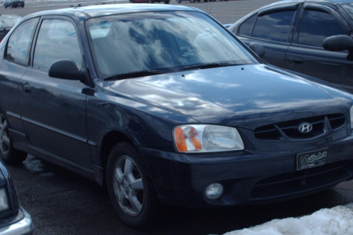 A dark navy blue Hyundai Accent hatchback parked in a lot with snow on the ground