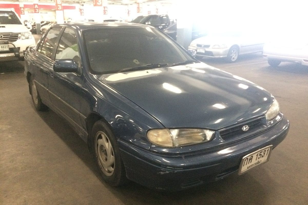 A dark blue first-generation 1993-1994 Hyundai Elantra sedan with a scuffed front bumper, parked in an indoor garage