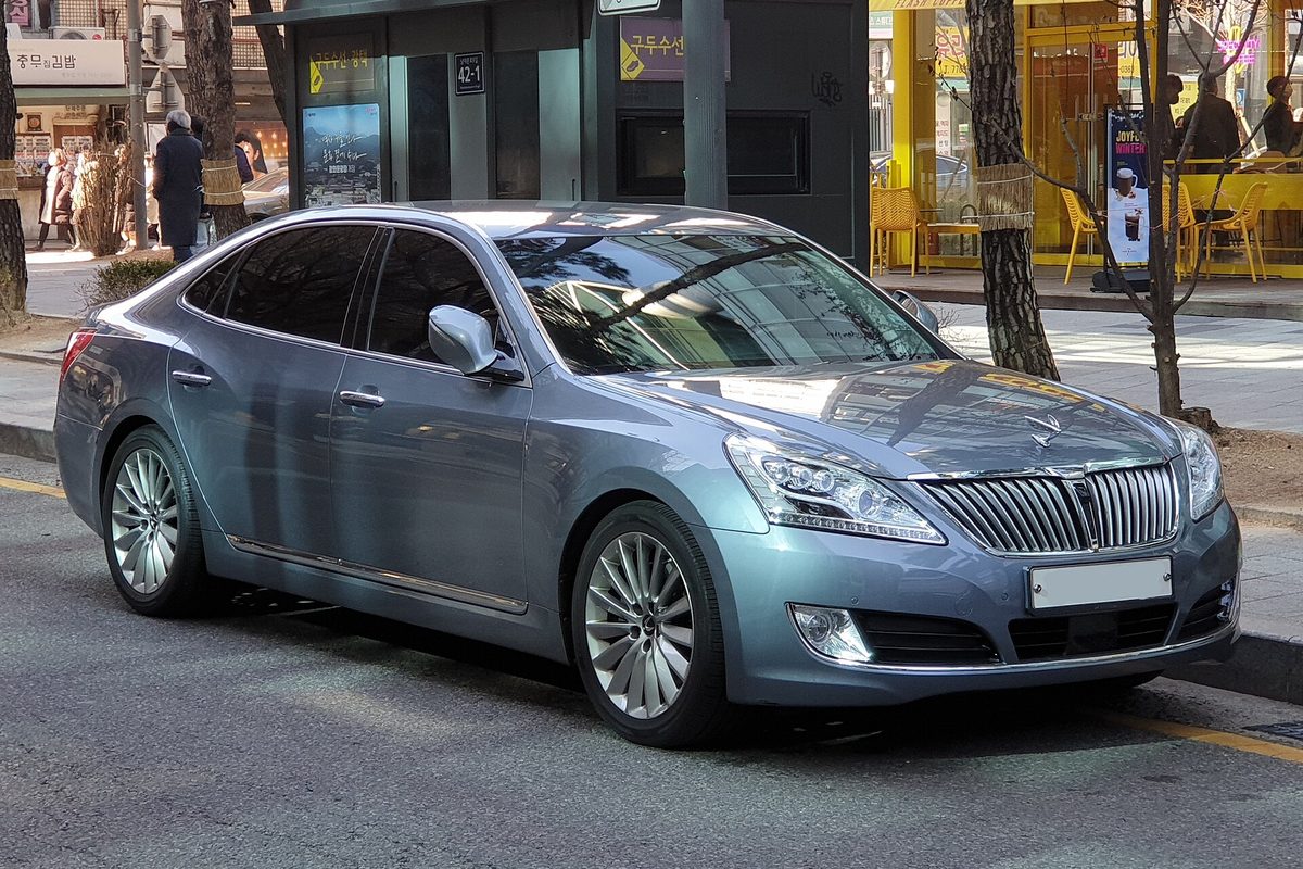 A blue-grey Hyundai Equus sedan with a tall vertical-bar grille, parked at a city curb by a cafe