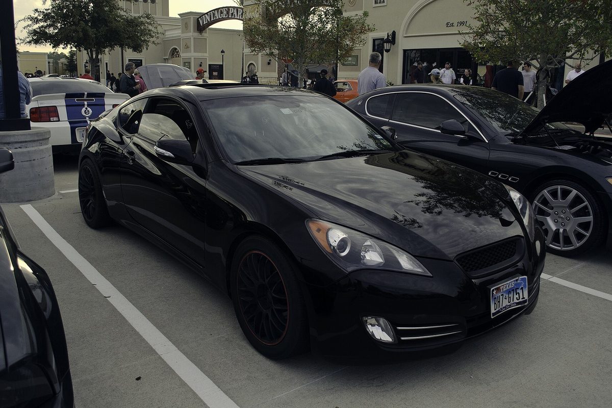 A black Hyundai Genesis Coupe with dark wheels, parked at an evening car meet