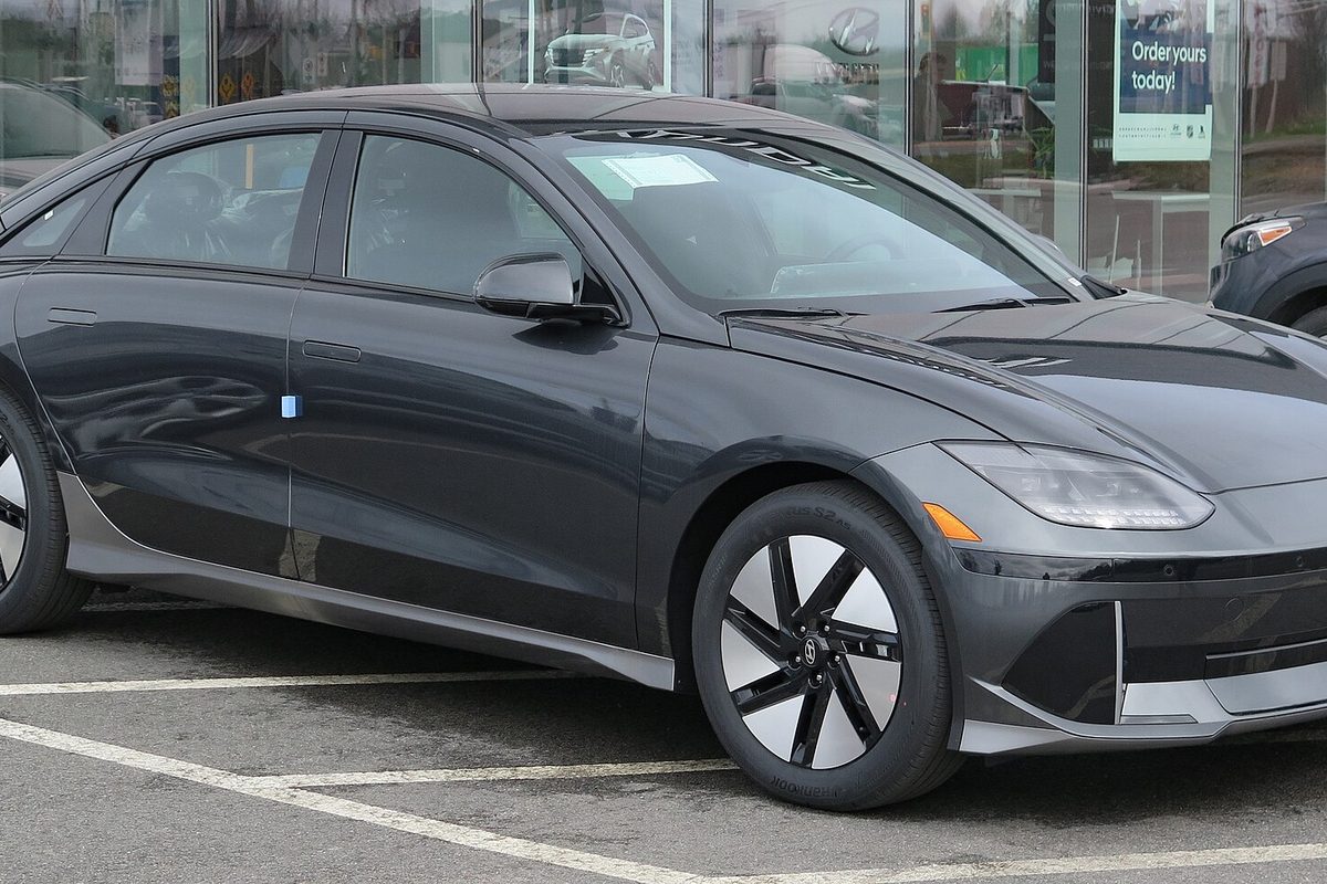 A dark gray Hyundai Ioniq 6 electric sedan, front right view, parked in front of a dealership showroom window