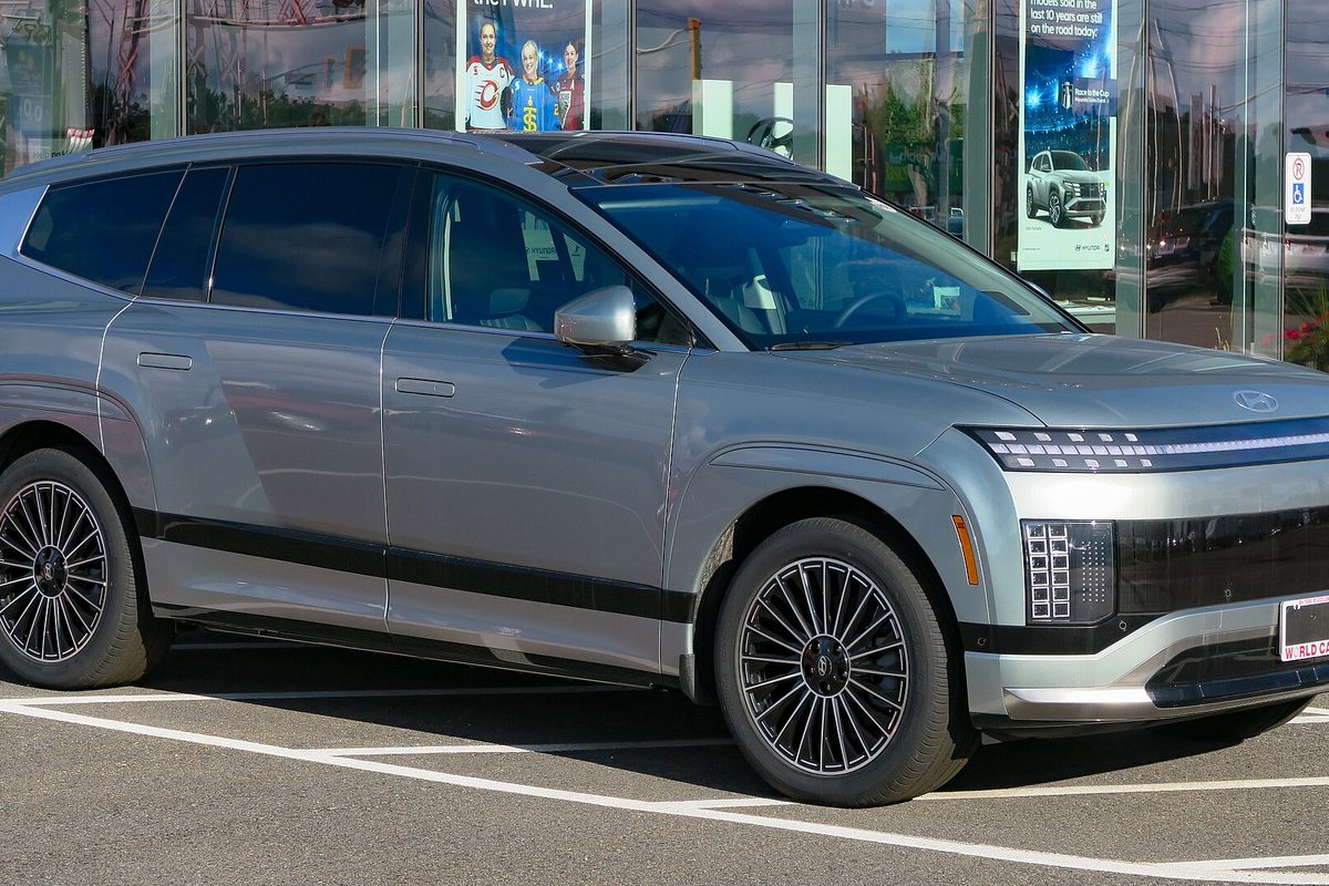 A grey Hyundai Ioniq 9 electric SUV with a light bar across the nose and multi-spoke wheels, parked outside a glass-fronted dealership