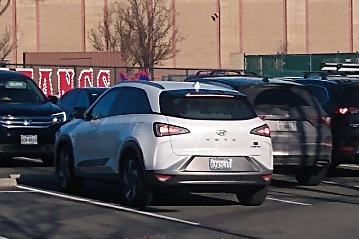 A white Hyundai Nexo fuel cell SUV seen from behind with its tail lights on, parked in a school parking lot
