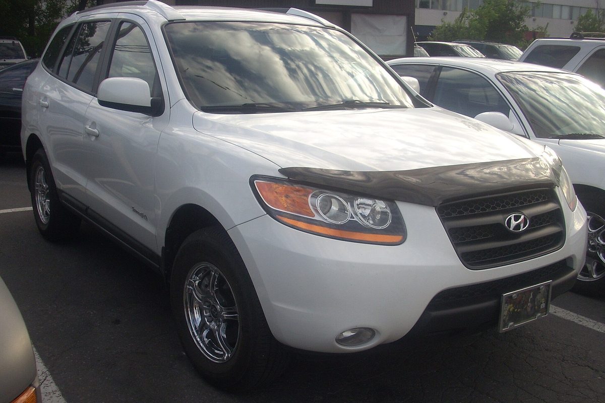 A white 2007-2009 Hyundai Santa Fe SUV with a dark hood deflector and chrome wheels, parked in a lot