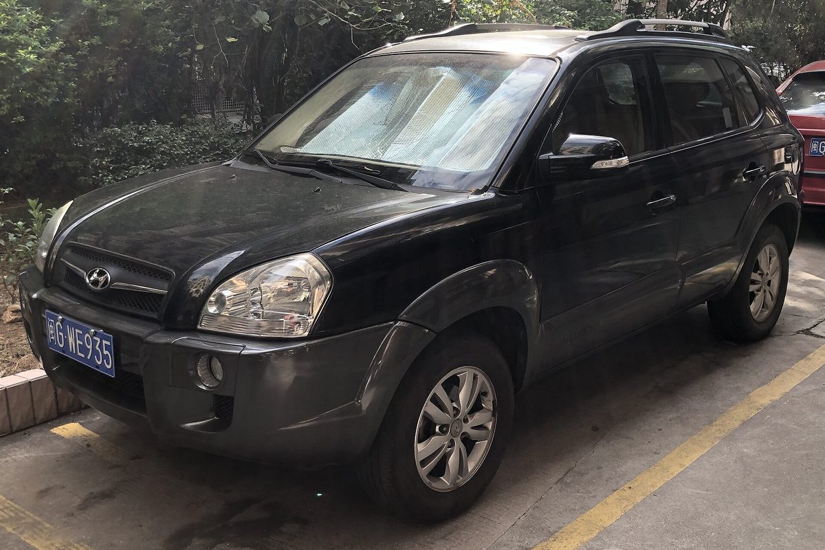 A black first-generation Hyundai Tucson compact SUV with roof rails and a sunshade in the windshield, parked beside a hedge