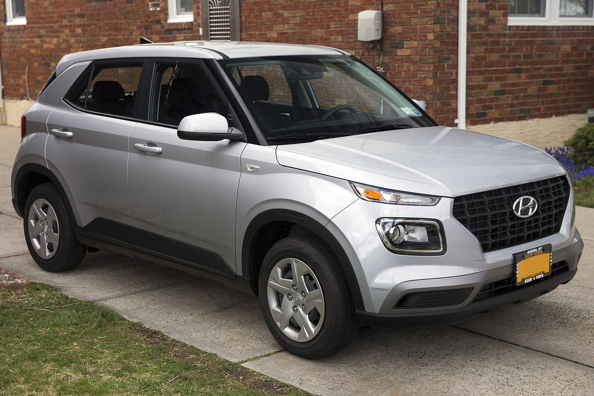 A silver Hyundai Venue small SUV, front right view, parked in a concrete driveway in front of a brick house