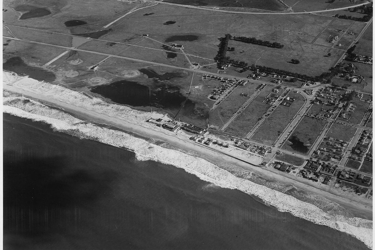 Black-and-white aerial photo of early Imperial Beach: surf along the shore, a strip of beachfront buildings and open fields crossed by a few streets of houses