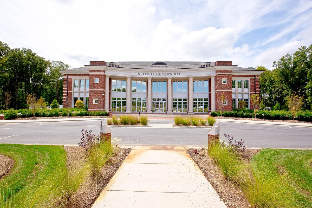 Indian Trail Town Hall, a brick building with white columns and tall windows, with a walkway lined by ornamental grasses