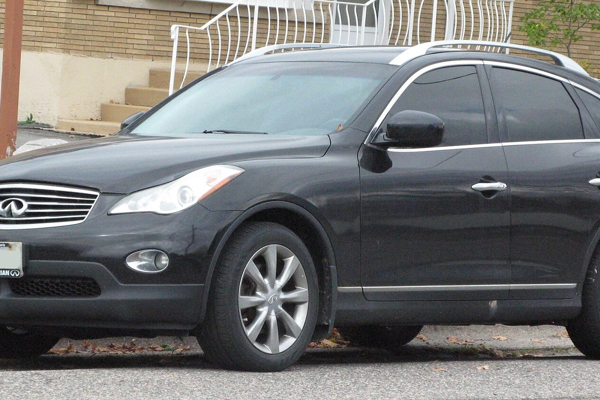 A dark gray 2012 Infiniti EX35 crossover with roof rails, parked on a street in front of a brick building's steps