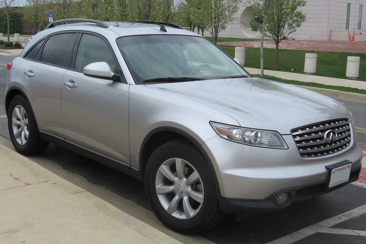 A silver first-generation Infiniti FX35 crossover parked at a curb next to a sidewalk and lawn