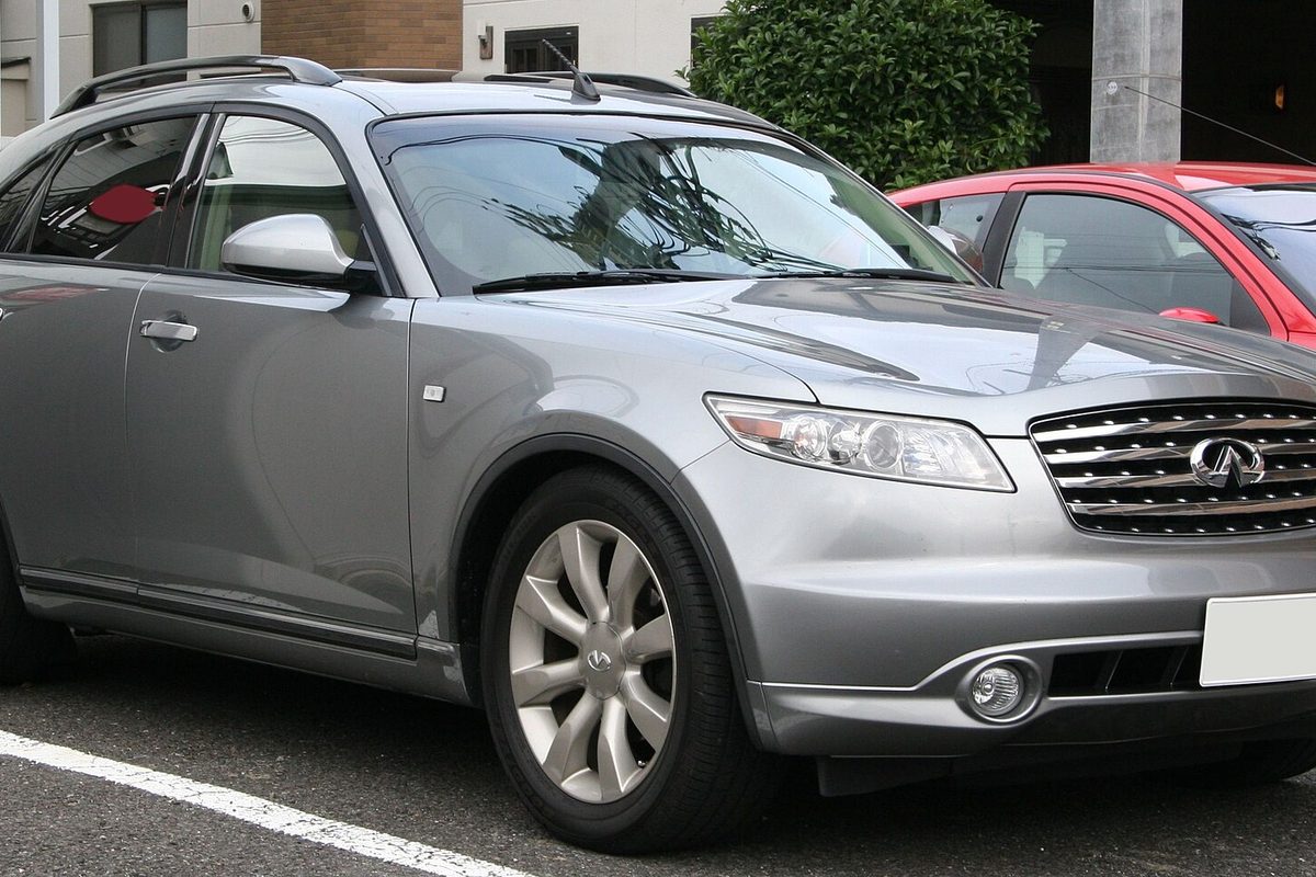 A silver first-generation Infiniti FX45 SUV parked in a lot, seen from the front right, with a red car behind it