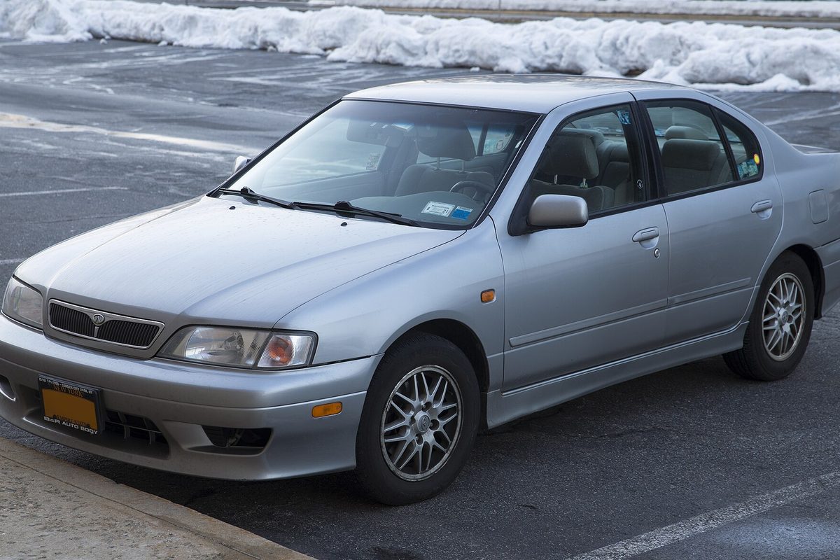 A silver 1999 Infiniti G20 sedan with alloy wheels, parked in a lot with plowed snowbanks behind it