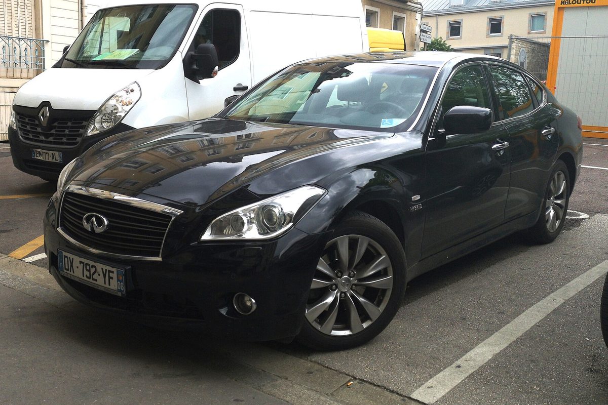 A black 2013 Infiniti M35h hybrid sedan parked on a city street next to a white van