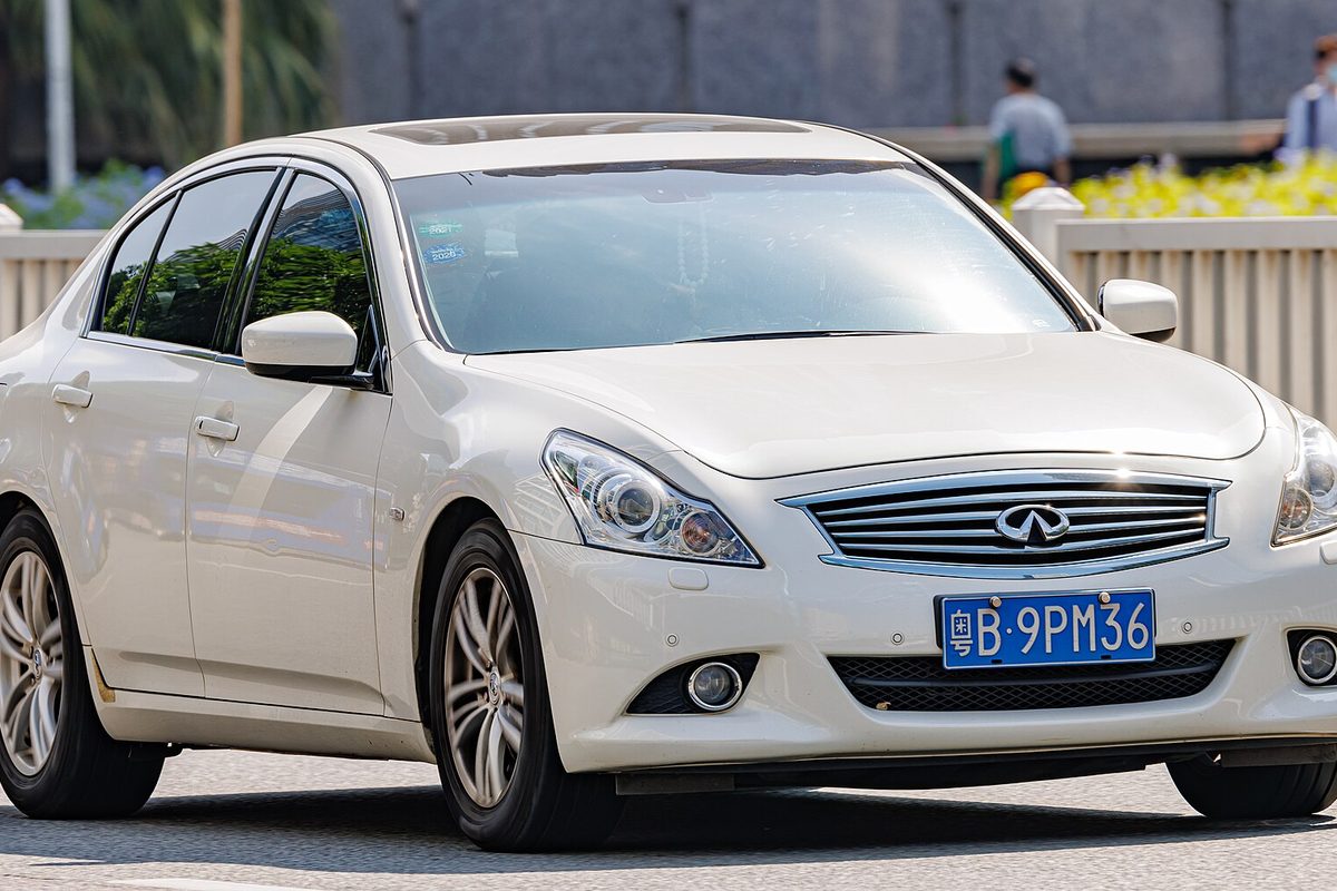 A pearl white Infiniti sedan of the V36 body, sold as the G and later the Q40, driving on a city street