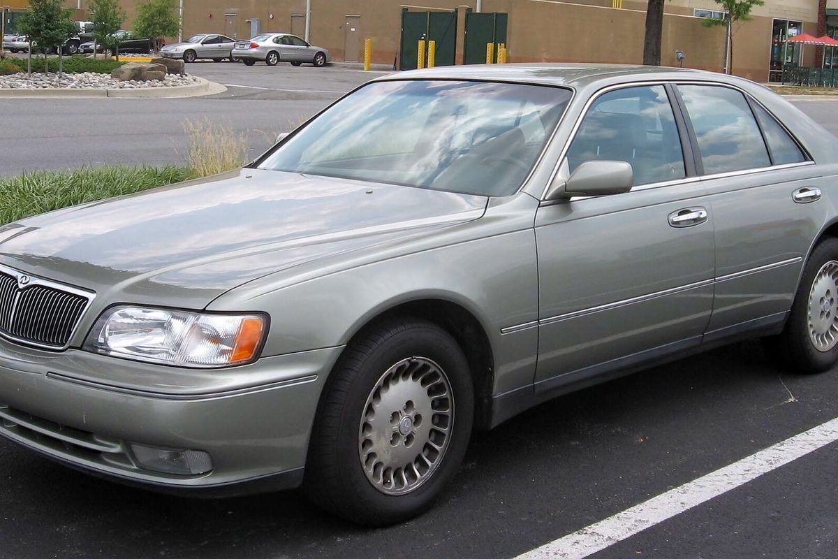 A gray-green Infiniti Q45 sedan with chrome grille and alloy wheels parked in a shopping center lot
