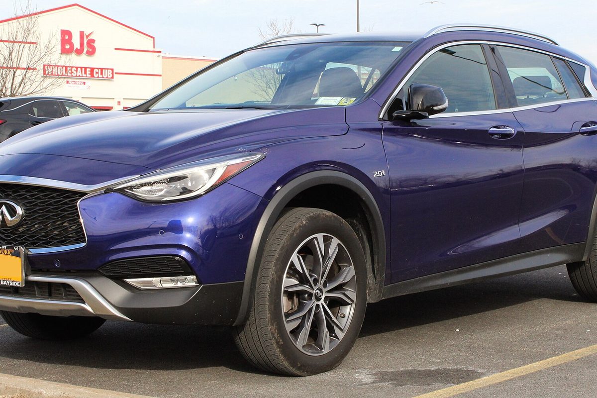 A dark blue 2017 Infiniti QX30 crossover with silver roof rails, parked in a store parking lot