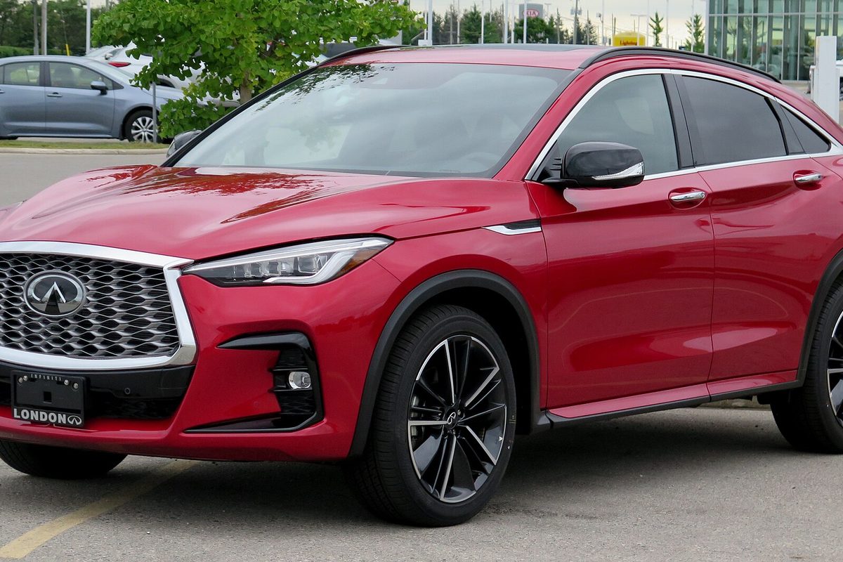 A red Infiniti QX55 coupe-style crossover with black wheels, parked in a lot beside a gray sedan
