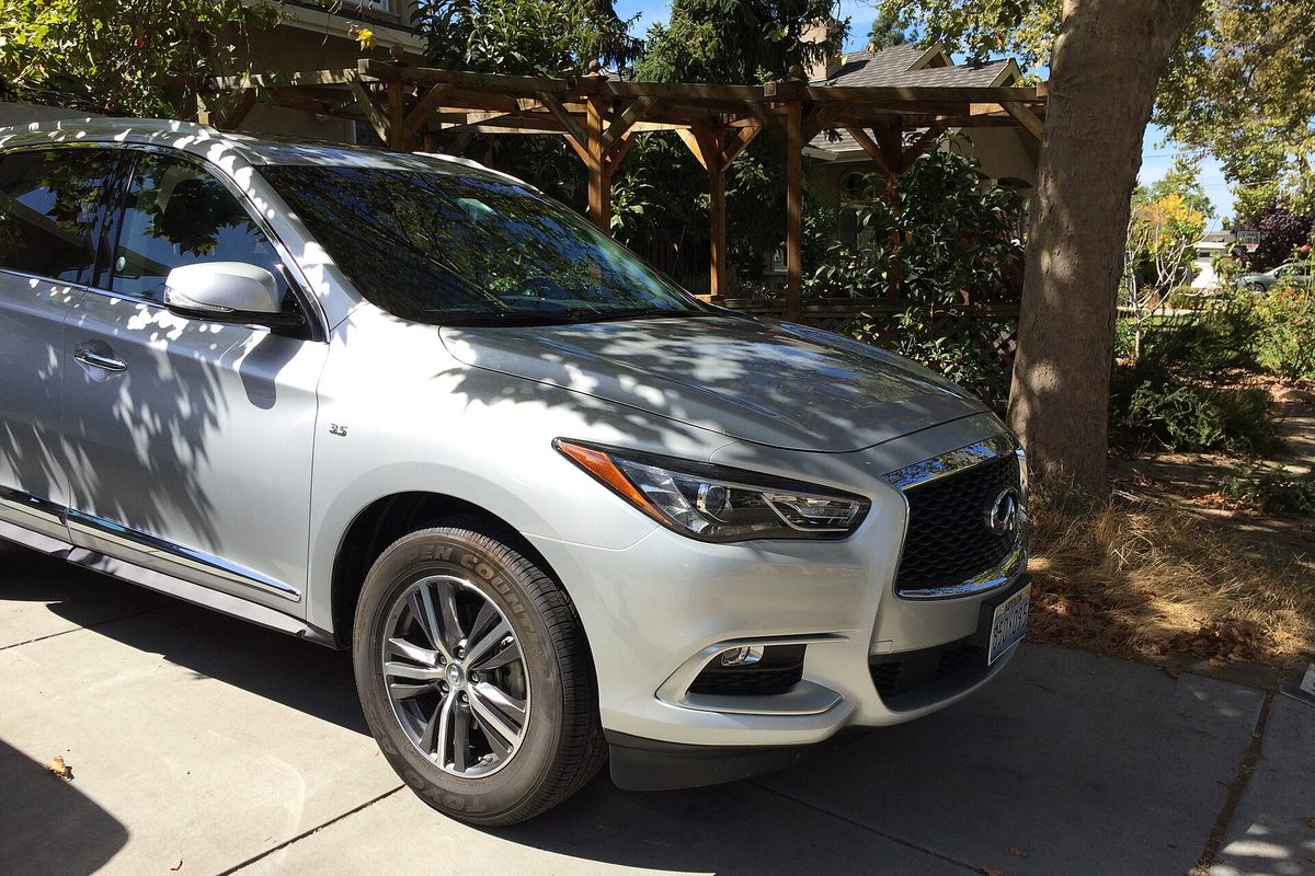 A silver 2016 Infiniti QX60 parked in a driveway under a tree, with a wooden pergola behind it