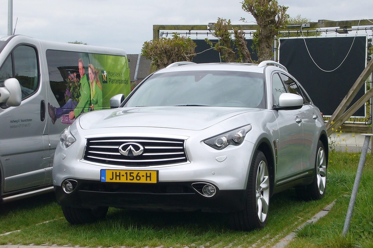A silver Infiniti QX70 crossover parked on grass beside a white van, seen from the front