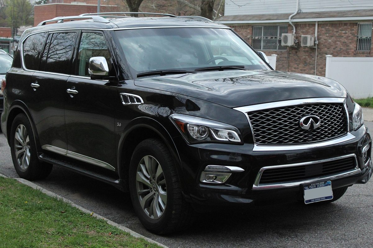 A black 2016 Infiniti QX80 parked at a curb in front of a brick house