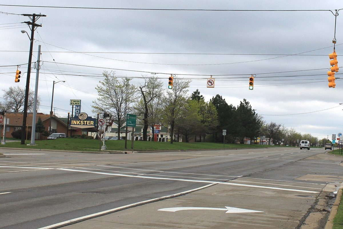 Michigan Avenue at Beech Daly Road in Inkster, a wide intersection with traffic lights hanging on wires and an Inkster sign on the grass under a gray sky