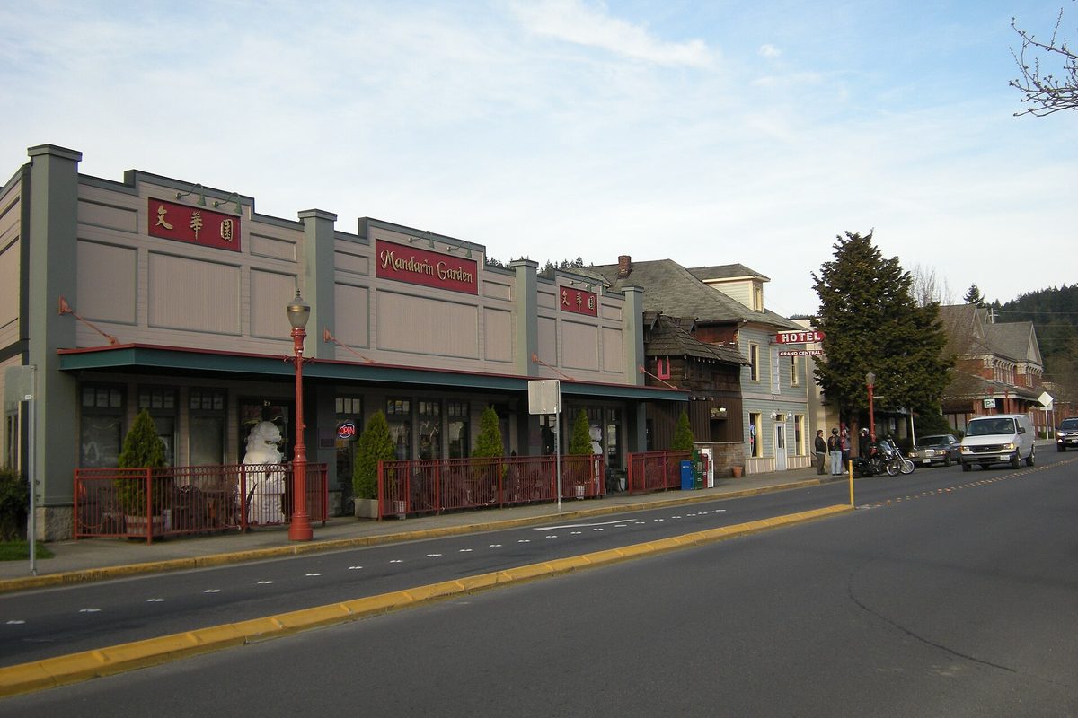 Shops along Sunset Way in Issaquah, including a restaurant with red signs and a red railing, a hotel sign and a pickup truck parked on the street