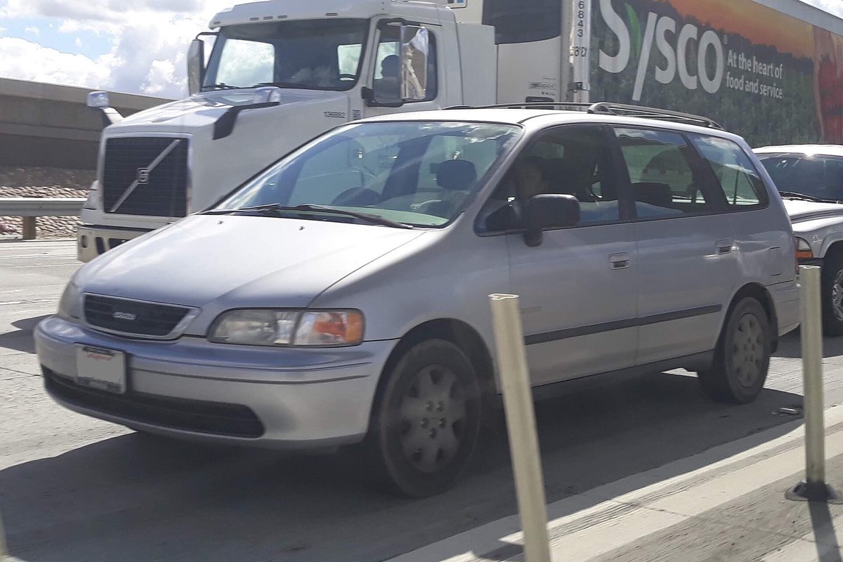 A silver Isuzu Oasis minivan driving in highway traffic beside a white semi truck