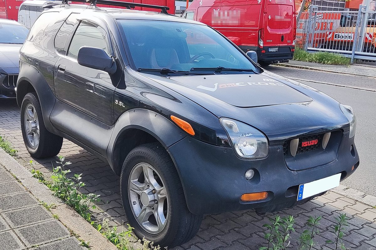 A black Isuzu VehiCROSS with dark gray lower body cladding, silver alloy wheels and a hood decal, parked on a brick-paved street