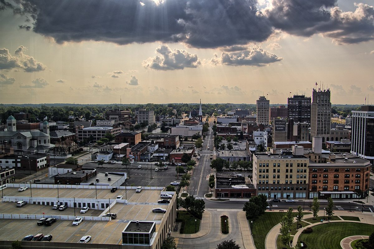 Downtown Jackson seen from the 12th floor of One Energy Plaza, with brick buildings, parking lots and a church spire under dark storm clouds
