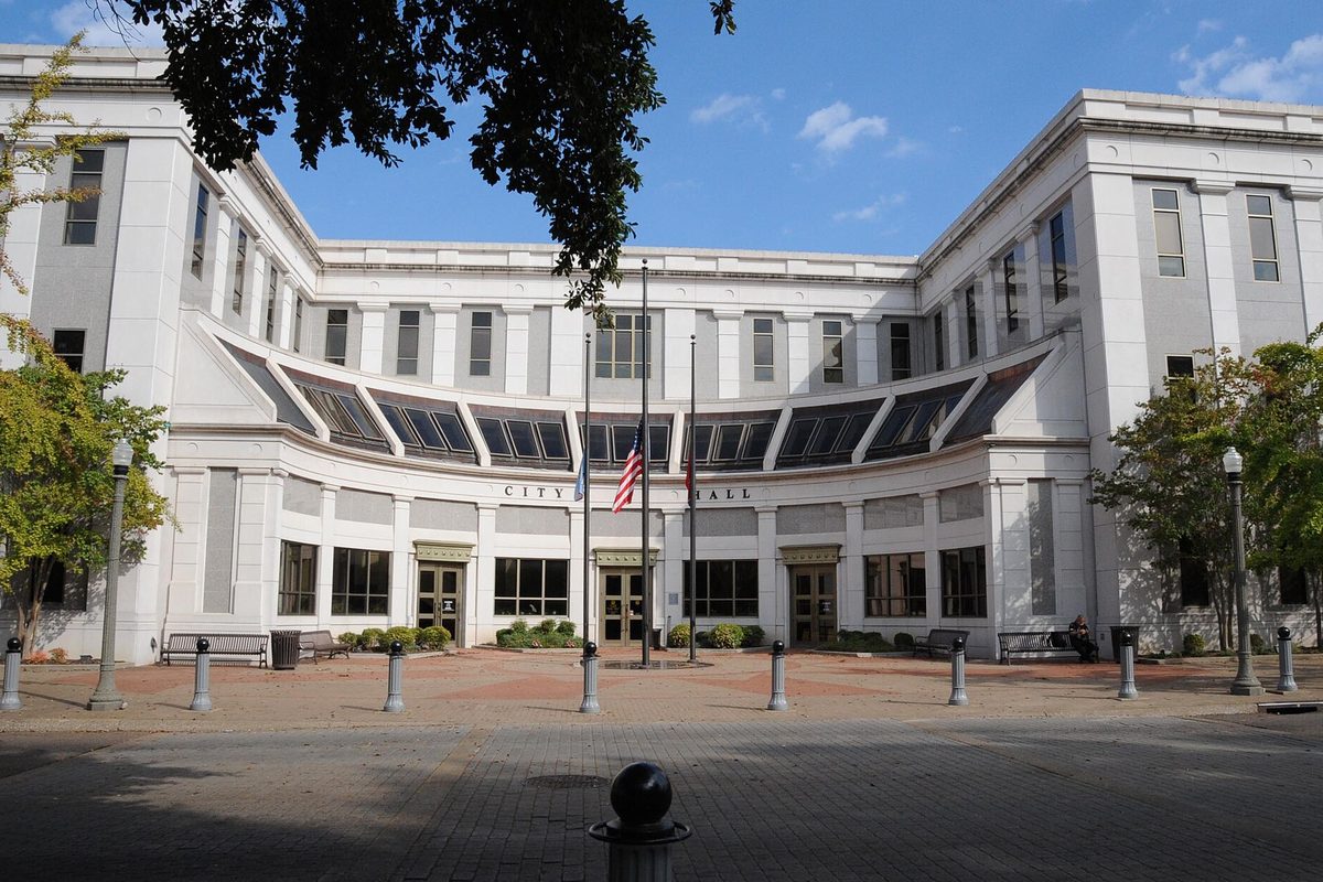 Jackson City Hall, a curved white building with tall windows and flags out front, across a brick plaza lined with bollards