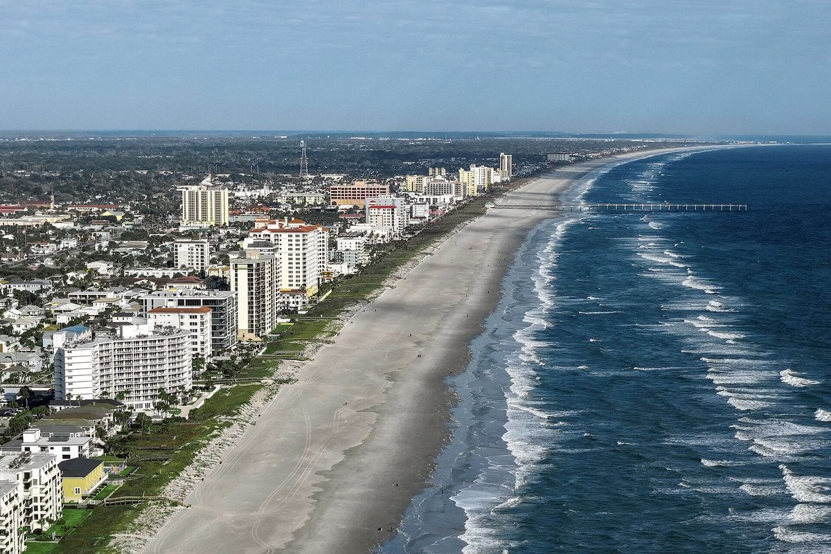 Aerial view of Jacksonville Beach, with high-rise condos along a wide sandy beach, Atlantic surf on the right and a long fishing pier in the distance