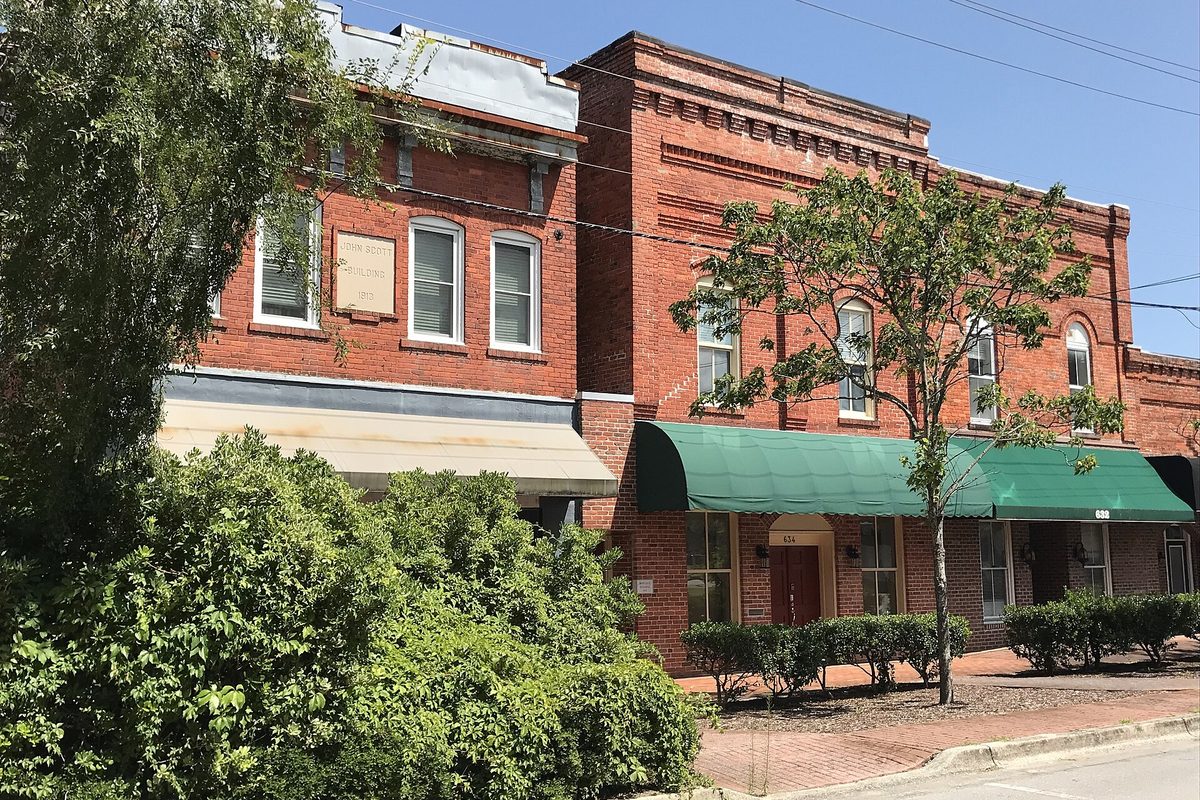 Two-story red-brick buildings on Court Street in Jacksonville, one with a green awning, behind a leafy tree and a brick sidewalk